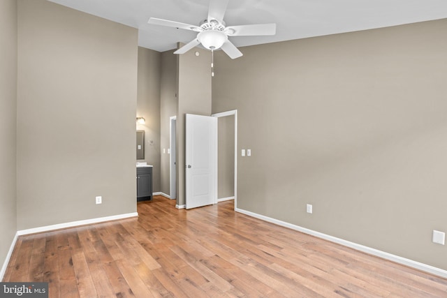 unfurnished bedroom with ceiling fan, ensuite bathroom, a towering ceiling, baseboards, and light wood-style floors