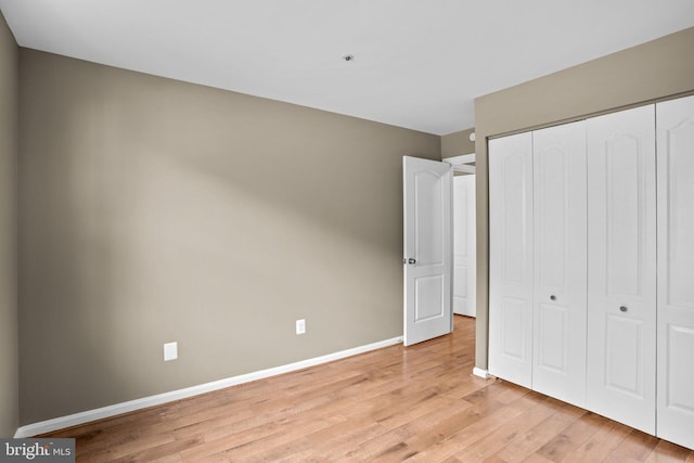 unfurnished bedroom featuring light wood-type flooring, baseboards, and a closet