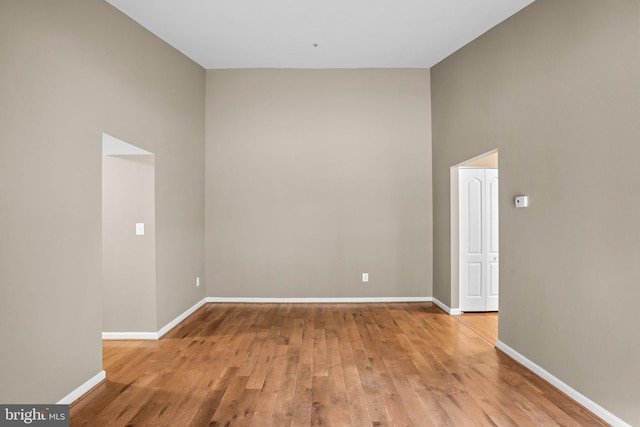 spare room with a towering ceiling, light wood finished floors, and baseboards