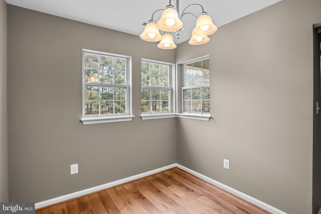 empty room with a chandelier, wood finished floors, and baseboards