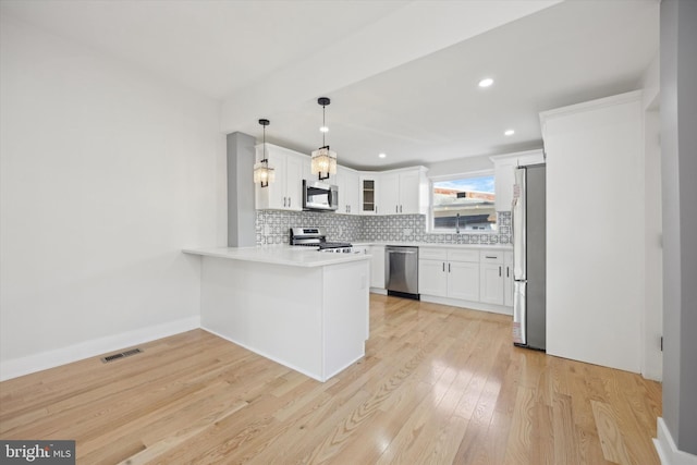 kitchen with kitchen peninsula, pendant lighting, stainless steel appliances, decorative backsplash, and white cabinets