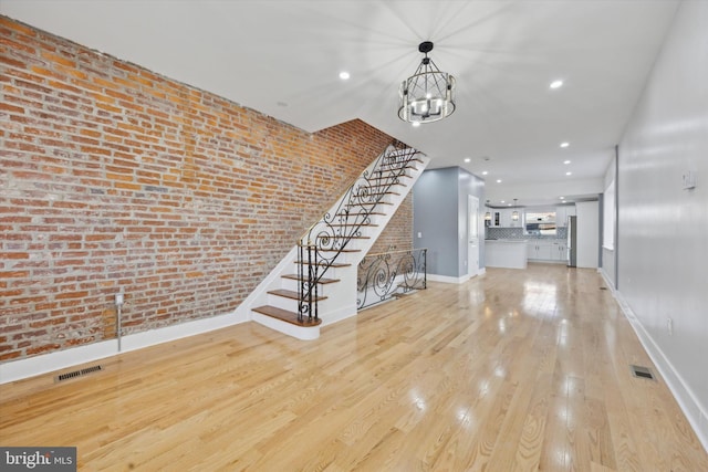 unfurnished living room featuring an inviting chandelier, brick wall, and light hardwood / wood-style floors