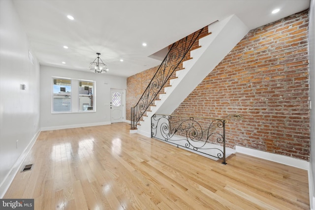 unfurnished living room with brick wall, light hardwood / wood-style floors, and a notable chandelier