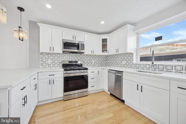 kitchen featuring sink, appliances with stainless steel finishes, white cabinetry, decorative light fixtures, and light wood-type flooring