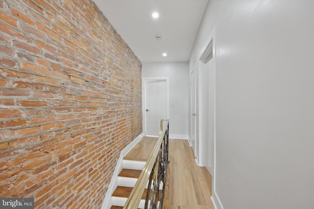 hall with light hardwood / wood-style floors and brick wall