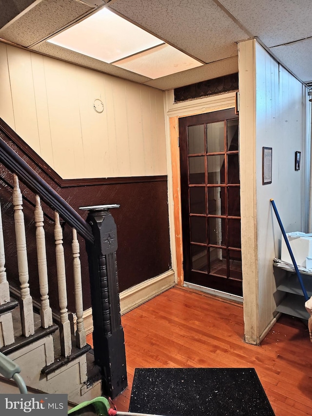 interior space with wooden walls, stairs, a drop ceiling, and wood finished floors