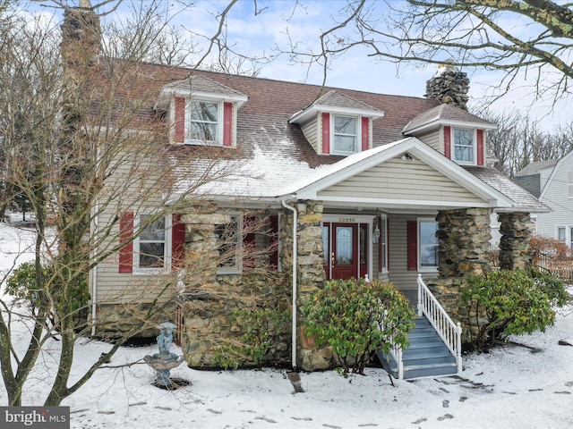 new england style home featuring a shingled roof, stone siding, and a chimney