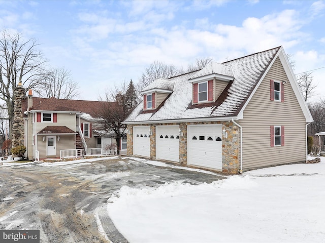 cape cod home with a garage and stone siding