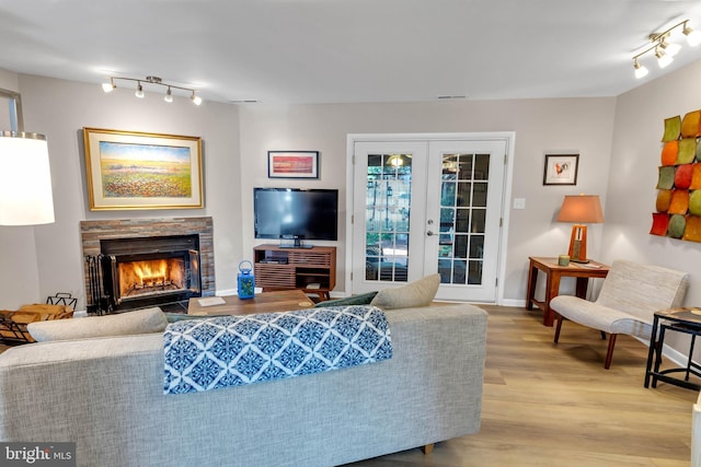 living room featuring a stone fireplace, track lighting, light hardwood / wood-style floors, and french doors