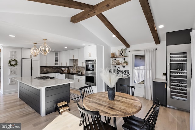 dining area featuring vaulted ceiling with beams, sink, beverage cooler, a chandelier, and light wood-type flooring