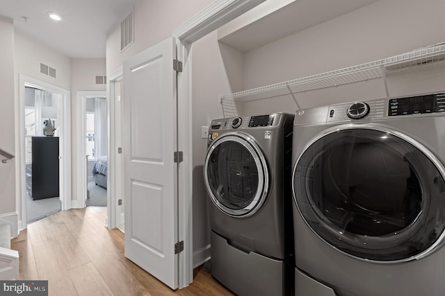 laundry area with washing machine and dryer and light hardwood / wood-style flooring