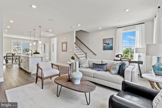 living room with an inviting chandelier, sink, and light wood-type flooring