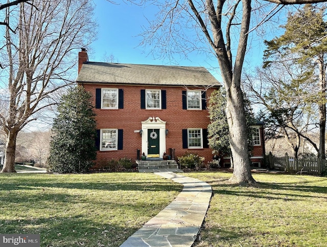 colonial home featuring a front yard, brick siding, and a chimney