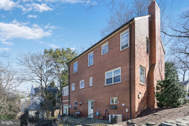 view of side of property featuring brick siding, a chimney, and central air condition unit