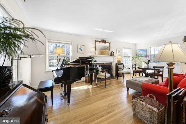 sitting room featuring a warm lit fireplace, ornamental molding, and light wood-type flooring