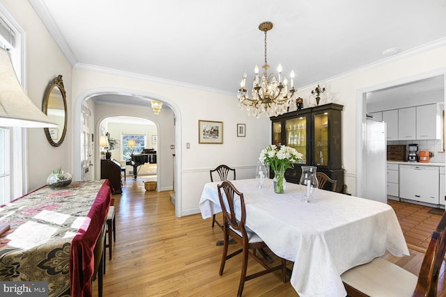 dining room with light wood-type flooring, arched walkways, a chandelier, and ornamental molding