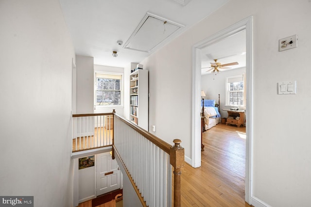 hall featuring attic access, baseboards, light wood-style flooring, and an upstairs landing