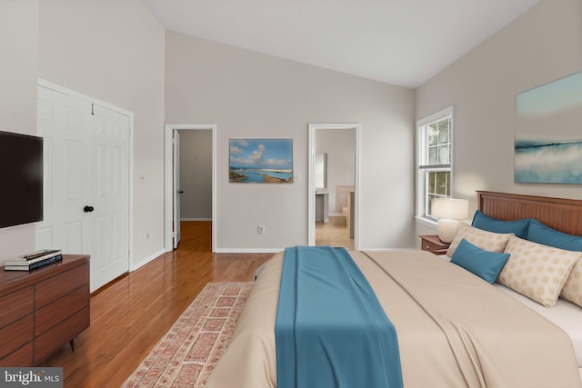 bedroom with baseboards, connected bathroom, lofted ceiling, light wood-style flooring, and a closet