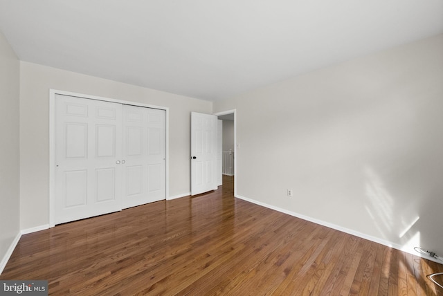 unfurnished bedroom with dark wood-style floors, a closet, and baseboards