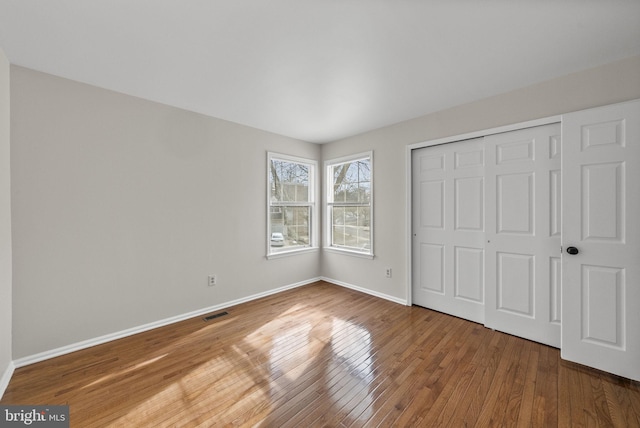 unfurnished bedroom featuring visible vents, a closet, baseboards, and wood finished floors