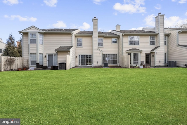 rear view of property featuring fence, central AC unit, and a lawn