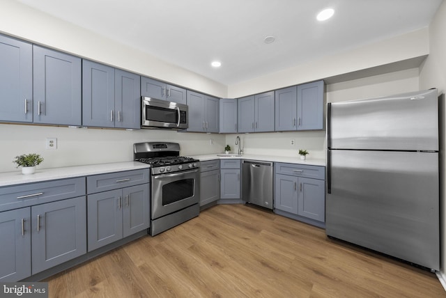 kitchen with appliances with stainless steel finishes, light countertops, light wood-type flooring, a sink, and recessed lighting