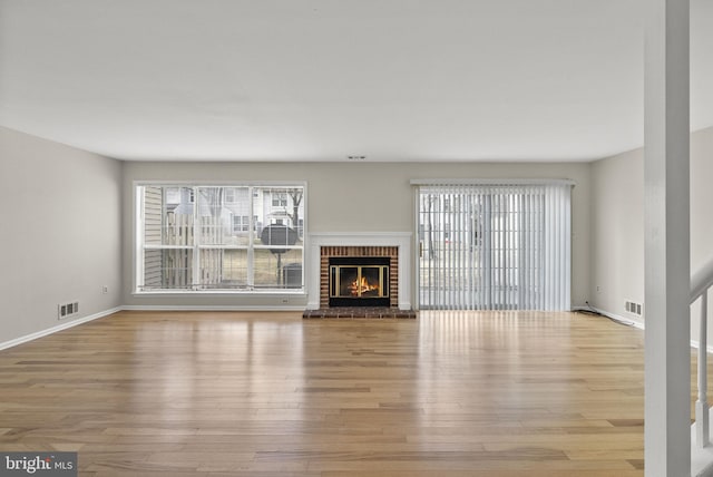 unfurnished living room with a brick fireplace, visible vents, and light wood-style floors