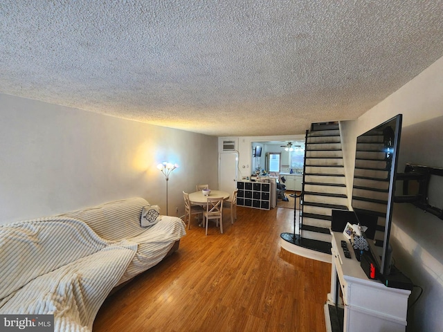 living room featuring ceiling fan, stairway, a textured ceiling, and wood finished floors