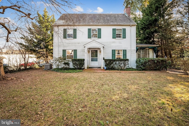 colonial inspired home featuring a front yard, fence, a chimney, and central air condition unit