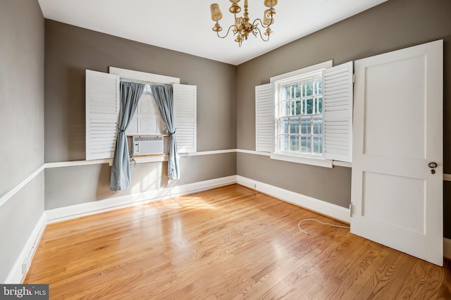 unfurnished room featuring cooling unit, baseboards, a chandelier, and wood finished floors