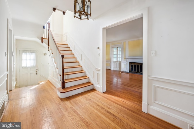 foyer featuring light wood finished floors, stairs, a decorative wall, and a glass covered fireplace