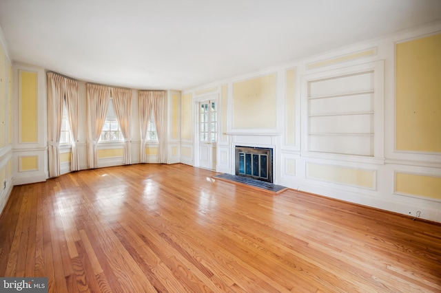 unfurnished living room with built in features, a glass covered fireplace, light wood-style floors, and a decorative wall