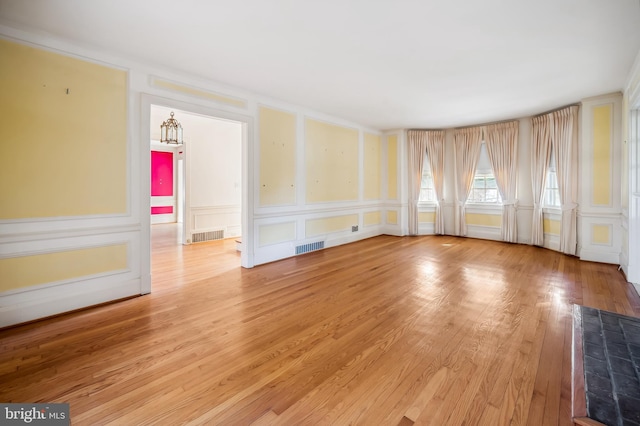 empty room featuring light wood-style floors, visible vents, and a decorative wall