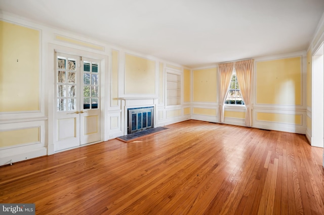 unfurnished living room featuring built in shelves, a glass covered fireplace, a decorative wall, and light wood finished floors