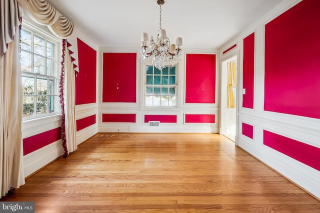 unfurnished dining area featuring wainscoting, a notable chandelier, visible vents, and wood finished floors