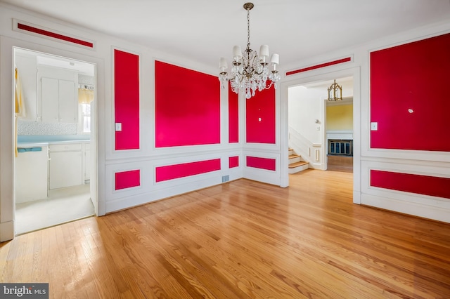 unfurnished dining area with a chandelier, a decorative wall, wood finished floors, and wainscoting