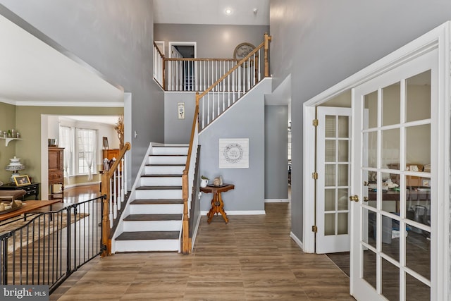 stairs featuring hardwood / wood-style flooring, ornamental molding, a towering ceiling, and french doors