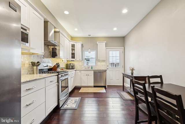 kitchen with pendant lighting, stainless steel appliances, glass insert cabinets, white cabinets, and wall chimney exhaust hood