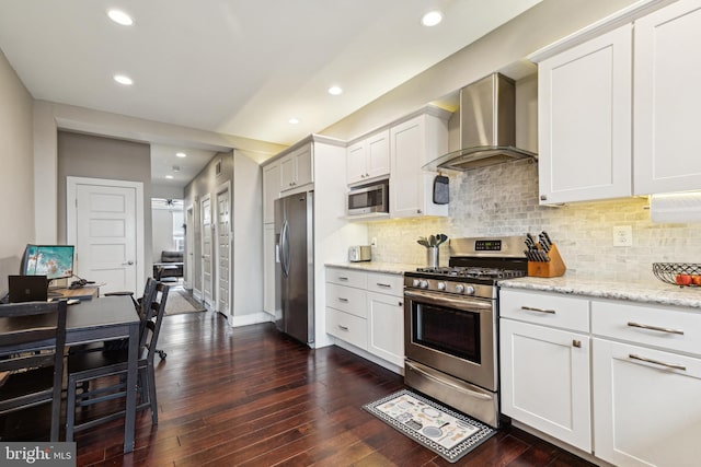 kitchen with stainless steel appliances, white cabinetry, light stone counters, and wall chimney exhaust hood