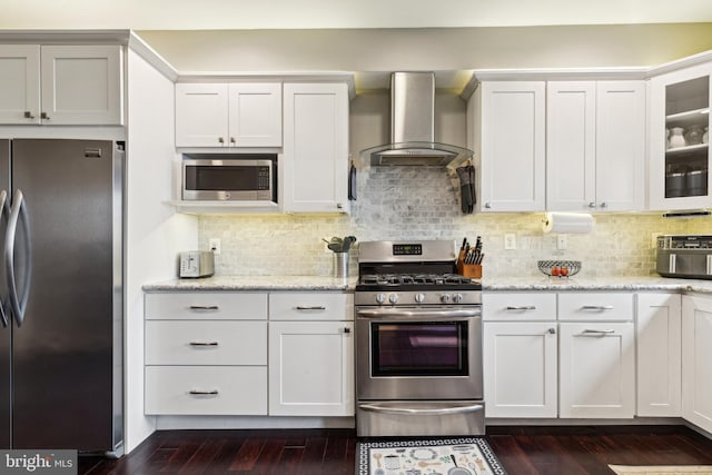 kitchen with white cabinets, wall chimney exhaust hood, glass insert cabinets, and stainless steel appliances