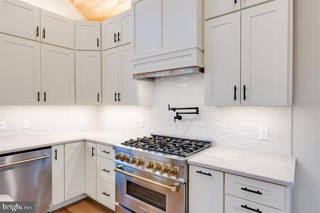 kitchen featuring vaulted ceiling, appliances with stainless steel finishes, white cabinetry, backsplash, and light stone countertops