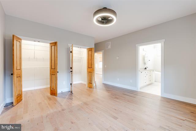 unfurnished bedroom featuring a spacious closet, light hardwood / wood-style floors, a closet, and ensuite bathroom