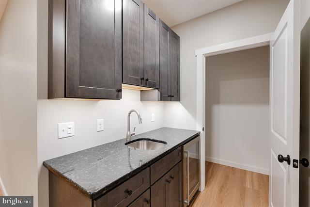 kitchen featuring sink, wine cooler, dark stone counters, dark brown cabinetry, and light hardwood / wood-style flooring