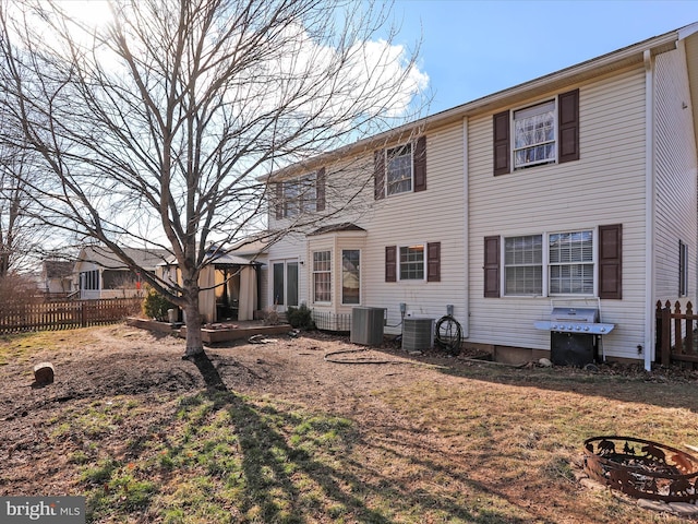 rear view of property with a lawn, a fire pit, and central air condition unit