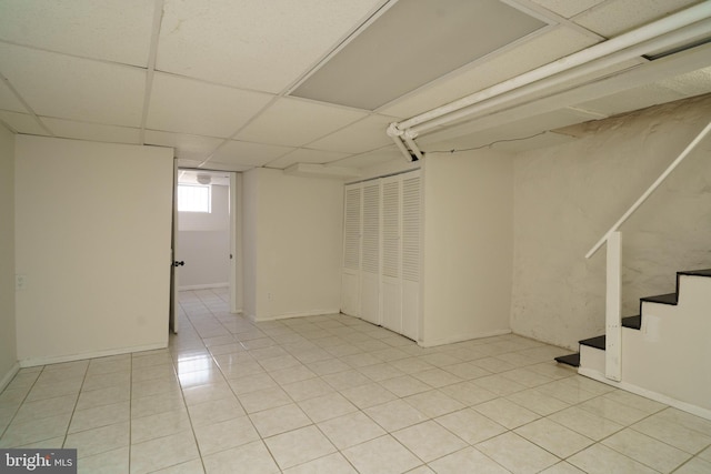 basement featuring stairs, a drop ceiling, and light tile patterned flooring