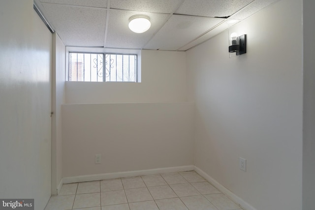 spare room with light tile patterned floors, baseboards, and a drop ceiling