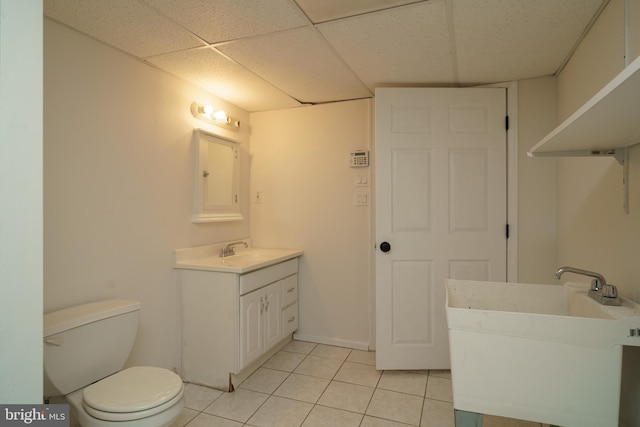 bathroom with a paneled ceiling, toilet, vanity, tile patterned flooring, and baseboards