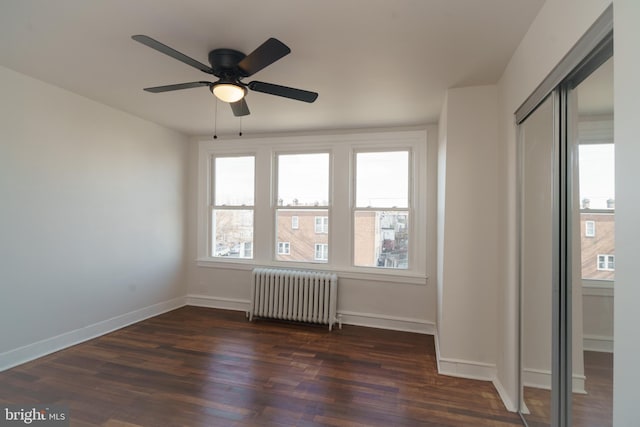 spare room with radiator, a ceiling fan, baseboards, and dark wood-type flooring