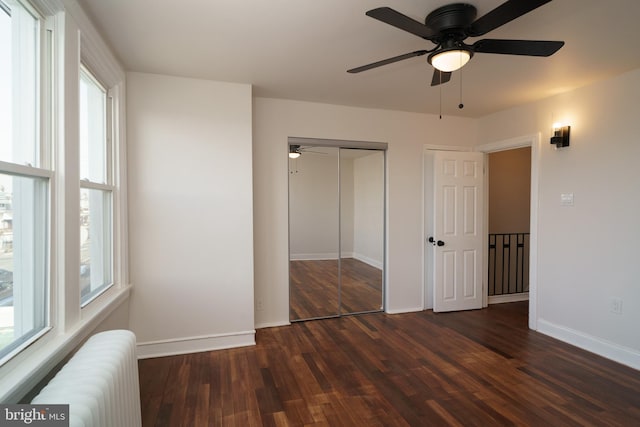 unfurnished bedroom with a ceiling fan, baseboards, a closet, radiator, and dark wood-style floors