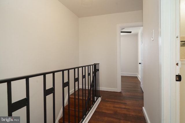 hall featuring dark wood-type flooring, an upstairs landing, and baseboards